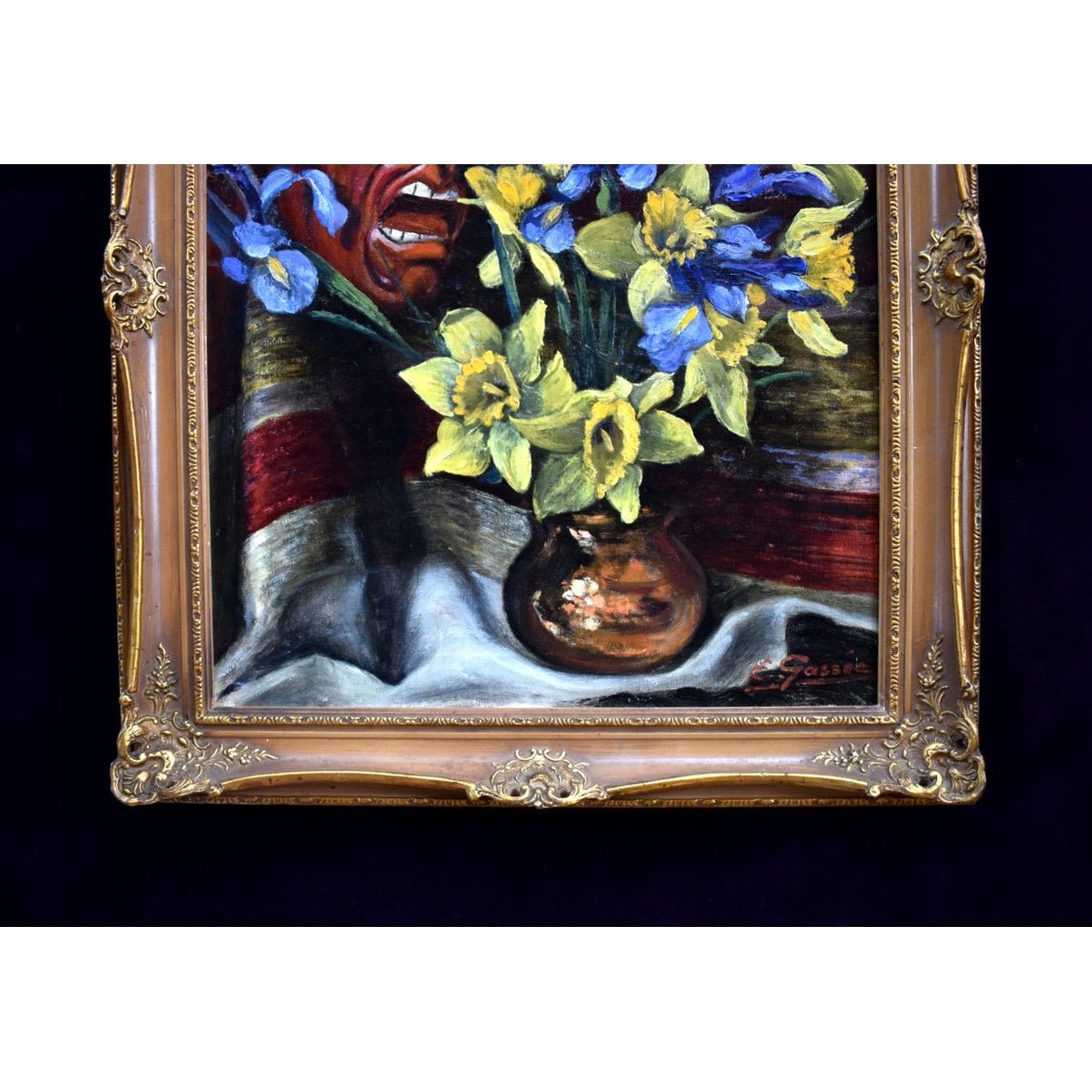 E. Gassée 1950s Belgian oil painting still life with red devil mask, blue irises, yellow daffodils in ornate gold baroque frame